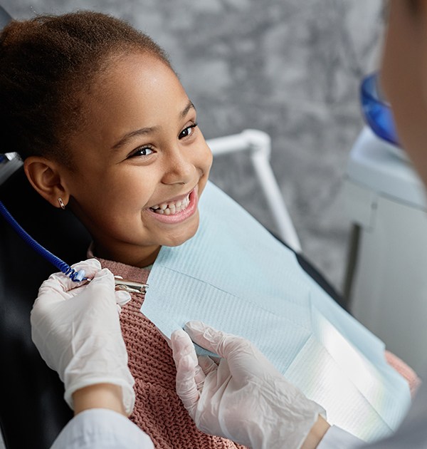 Little girl in pink sweater in dental chair preparing for checkup