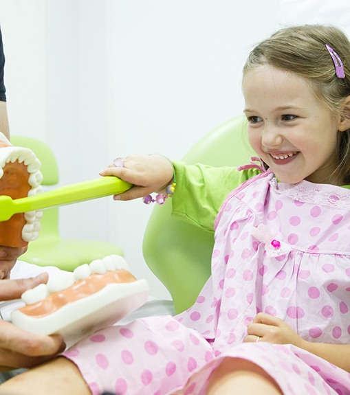 Little girl in dental chair brushing giant teeth with giant toothbrush