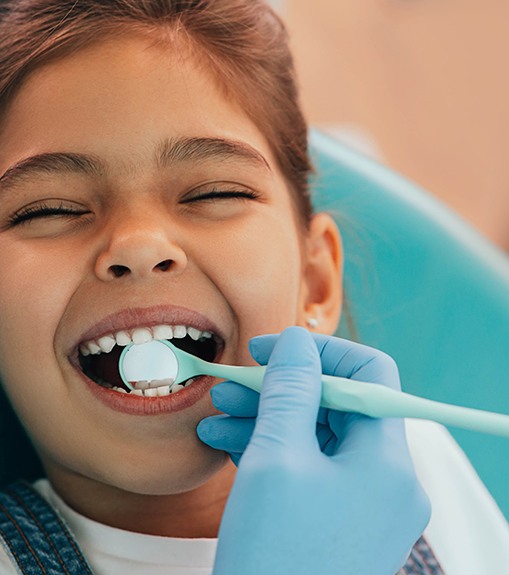 Little girl biting down on dental mirror in her mouth